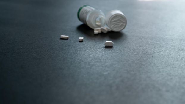 White tablets pills and blur plastic pill bottle on dark floor. Prescription drugs. Pharmaceutical industry. Medical care. Medication for cure illness. Pharmacy. Small white pills. Dose recommended.