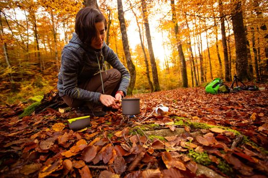 Woman uses portable gas heater and pan for cooking outdoors while camping. Collapsible bottles to save space in your backpack.