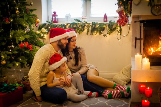 Happy family - parents and children sitting by fireplace on Christmas Eve