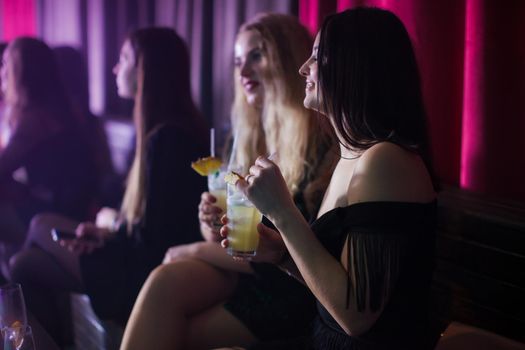 Women have fun and drinking cocktails with fruits in night club. Dance party