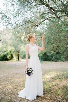 Bride with a bouquet of flowers stands near an olive tree. High quality photo