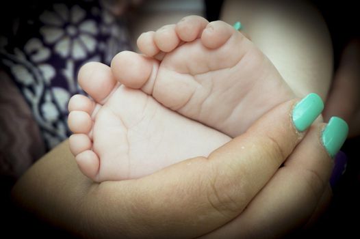 Baby feet held by mothers hand. Black background