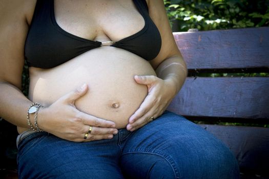 Seven month pregnant woman in a park dressed in jeans