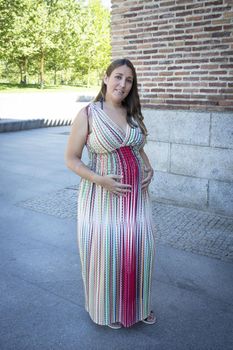 Seven month pregnant woman outdoors in multi colored striped dress. Day scene