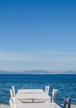 White restaurant tables on the beach in summer - travel, vacation and summer concept. The perfect lunch with a sea view