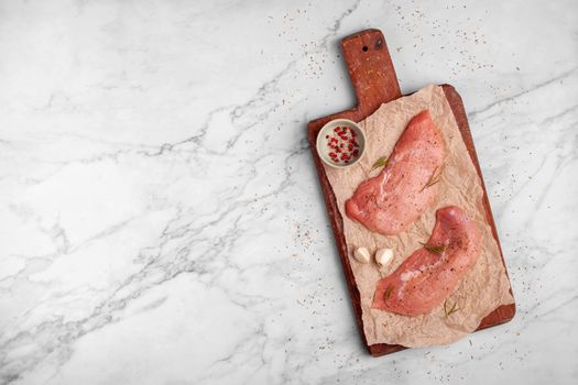 two raw veal escalope on the old wooden cutting board, ready to cook, marbre background, top view, copy space