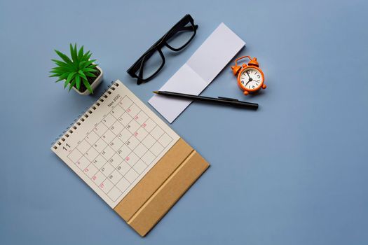 November 2022 desk calendar with alarm clock set at 9 o'clock and notepad on blue background. Directly above. Flat lay. Copy space.