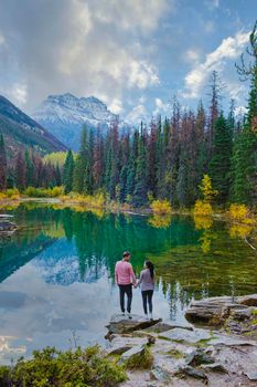 Horseshoe lake Jasper Canadian Rockies Alberta Canada, colorful autumn trees reflected in the lake. Couple Asian women and caucasian men on vacation in Canada standing by a lake with autumn trees