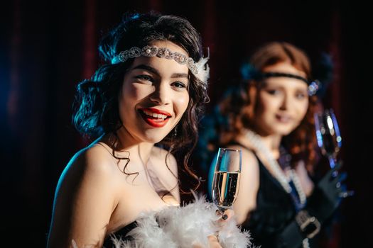 Portrait of young flapper women dressed in style of Great Gatsby posing on dark velours background. Roaring twenties, retro, party, fashion concept.