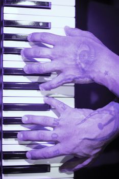 Tattooed mans hands on the keyboard of a piano. Dark background