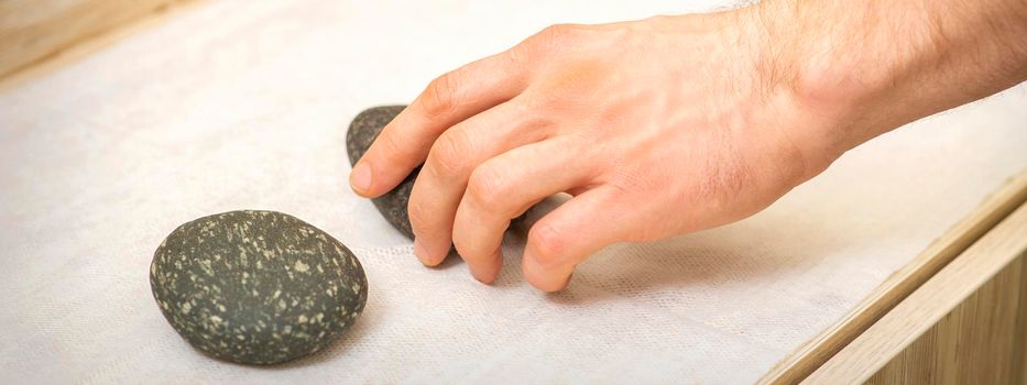 Hand of massage therapist taking massage stones from the table before massage procedures