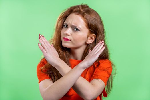 Pretty woman disapproving with no crossing hands sign make basta, negation, enough gesture. Denying, Rejecting, Disagree, Portrait of pretty girl on green background. High quality photo