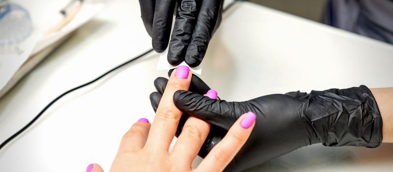 Manicurist applies a matte coating with a napkin on female pink nails in a nail salon