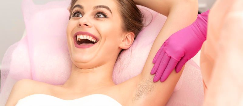 Young woman during armpit examination before waxing procedure laughing in a beauty salon