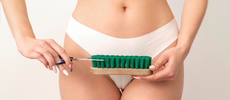 Epilation concept. A young caucasian woman wears white panties is cutting a cleaning brush with scissors standing on white background