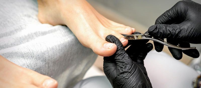 Closeup of a pedicure master is cutting and removing cuticle with nail tongs on female toes in a nail salon