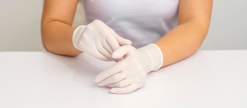 Two hands in white protective gloves of nurse or female doctor sitting at the white table