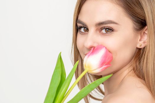 Beautiful caucasian young woman with one tulip against a white background