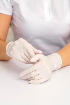 Two hands in white protective gloves of nurse or female doctor sitting at the white table