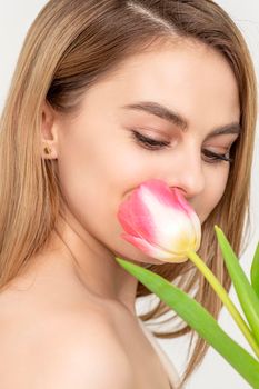 Beautiful caucasian young woman with one tulip looking on a flower against a white background