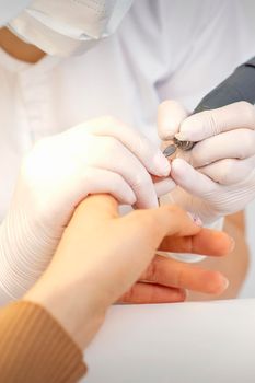 Closeup of manicure master removes nail polish uses an electric nail file in a nail salon