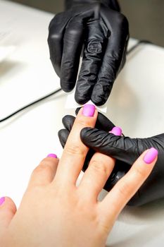 Manicurist applies a matte coating with a napkin on female pink nails in a nail salon