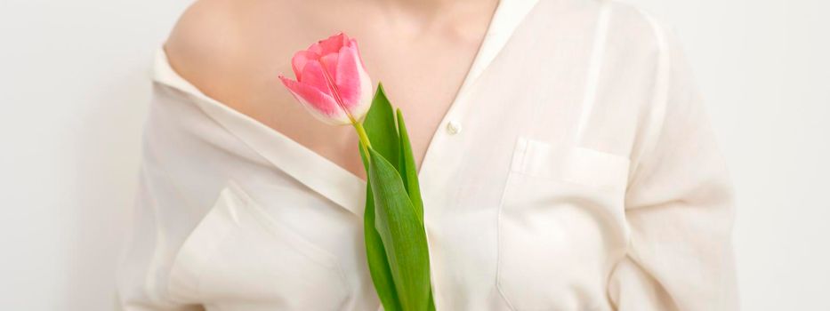 Beautiful young unrecognizable female with one tulip against a white background