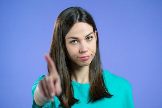 Portrait of serious woman showing rejecting gesture by stop finger sign. Girl isolated on violet background. High quality photo