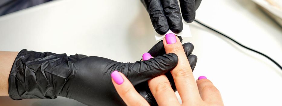 Manicurist applies a matte coating with a napkin on female pink nails in a nail salon