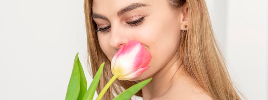 Beautiful caucasian young woman with one tulip looking on a flower against a white background