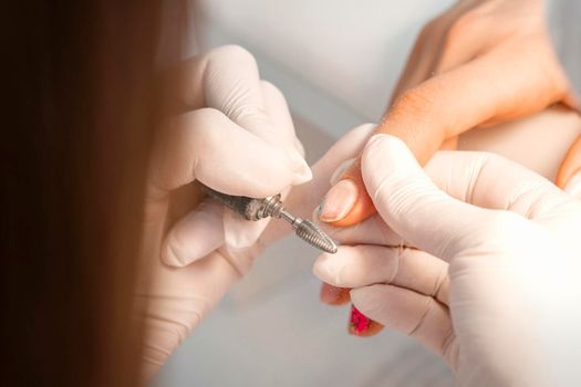 Closeup of manicure master removes nail polish uses an electric nail file in a nail salon