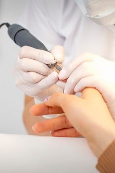 Closeup of manicure master removes nail polish uses an electric nail file in a nail salon