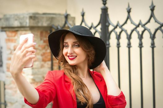 Beautiful smiling caucasian young woman taking selfie on the smartphone against an urban background