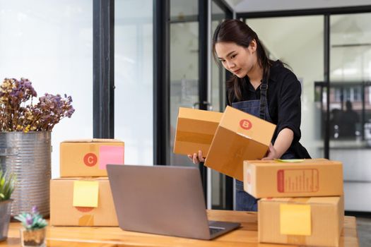 Business woman owner holding parcel box for delivery and using laptop at home office. Entrepreneur small business working at home