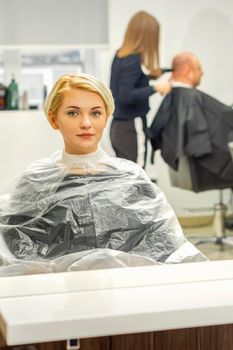 Young female client waiting for the hairdresser looking in the mirror in a hair salon