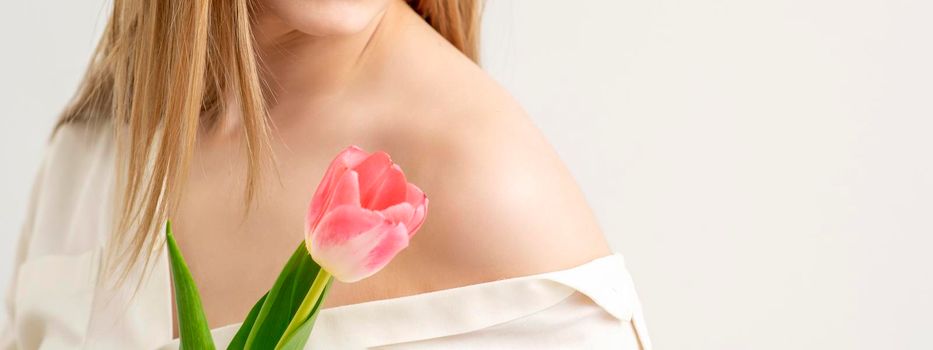 Beautiful young unrecognizable female with one tulip against a white background