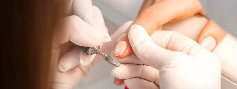 Closeup of manicure master removes nail polish uses an electric nail file in a nail salon