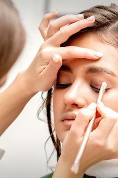 Makeup artist applies eye shadow with a brush on the eye of a beautiful young caucasian woman against a white background