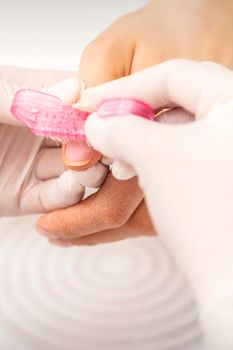 Closeup of manicurist is brushing dust with a pink plastic brush from female fingernails in a nail salon