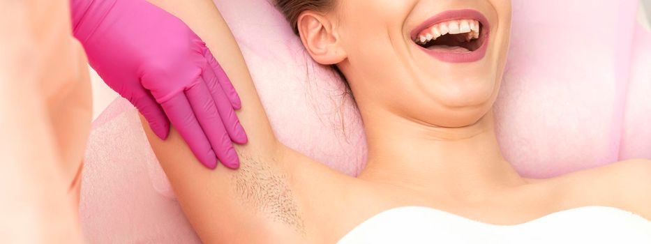 Young woman during armpit examination before waxing procedure laughing in a beauty salon
