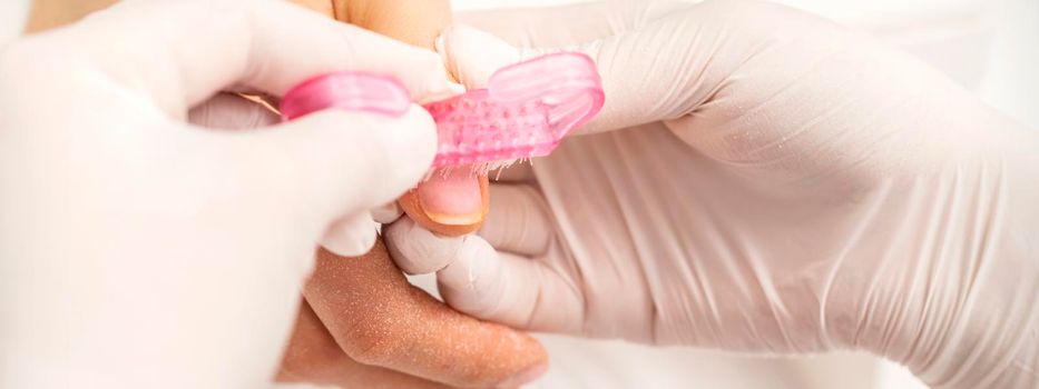 Closeup of manicurist is brushing dust with a pink plastic brush from female fingernails in a nail salon
