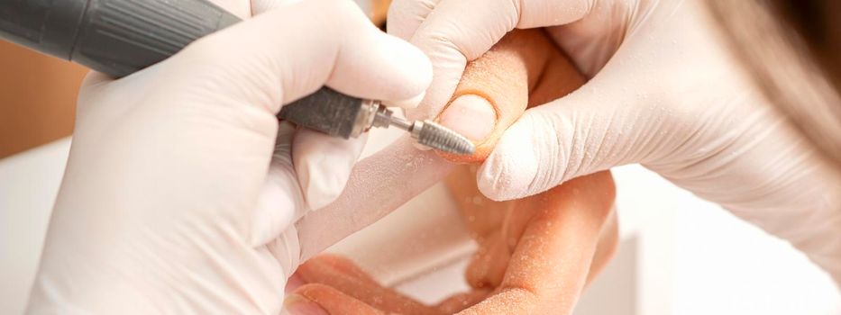 Closeup of manicure master removes nail polish uses an electric nail file in a nail salon