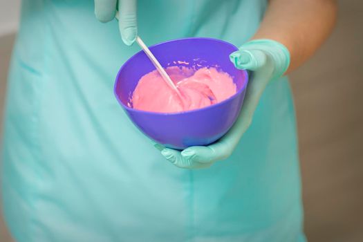 Close up of beautician's hands prepares pink alginate mask mixing in the blue bowl