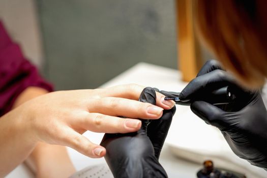Close up of manicure master covering nails with the transparent polish of female nails in a nail salon