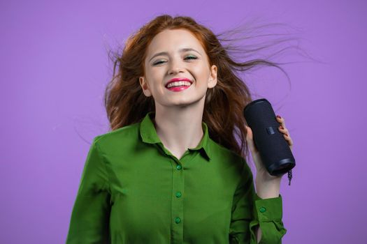 Woman listening to music by wireless portable speaker - modern sound system. Lady dancing, enjoying on violet studio background. She moves to the rhythm of music. High quality photo