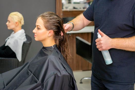 Male hairdresser sprays water long wet hair of a young woman in a hair salon