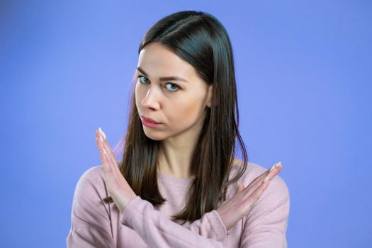 Pretty girl disapproving with no crossing hands sign make basta, negation, enough gesture. Denying, Rejecting, Disagree, Portrait of pretty girl on violet background. High quality photo