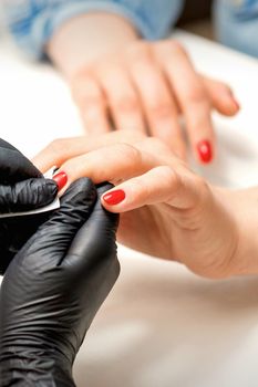 Close up of manicure master leaks female red nails with a lint-free napkin in a nail salon