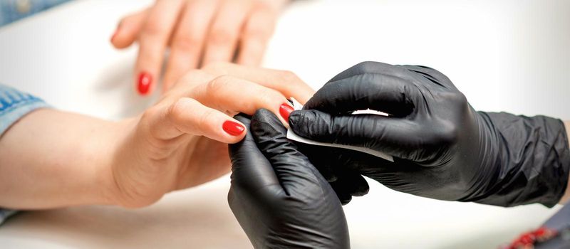 Close up of manicure master leaks female red nails with a lint-free napkin in a nail salon