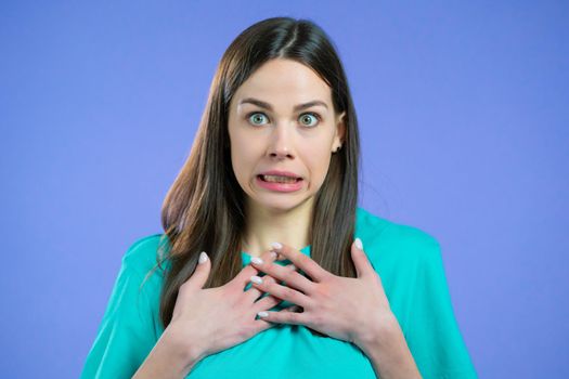 Portrait of unpleasantly surprised and shocked girl on violet studio background. Woman receiving bad news. She expresses sympathy and regret. High quality photo